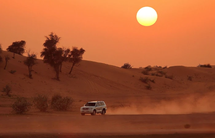 Evening Desert Safari Dubai – breathtaking golden sunset over red sand dunes with Bedouin camp in background